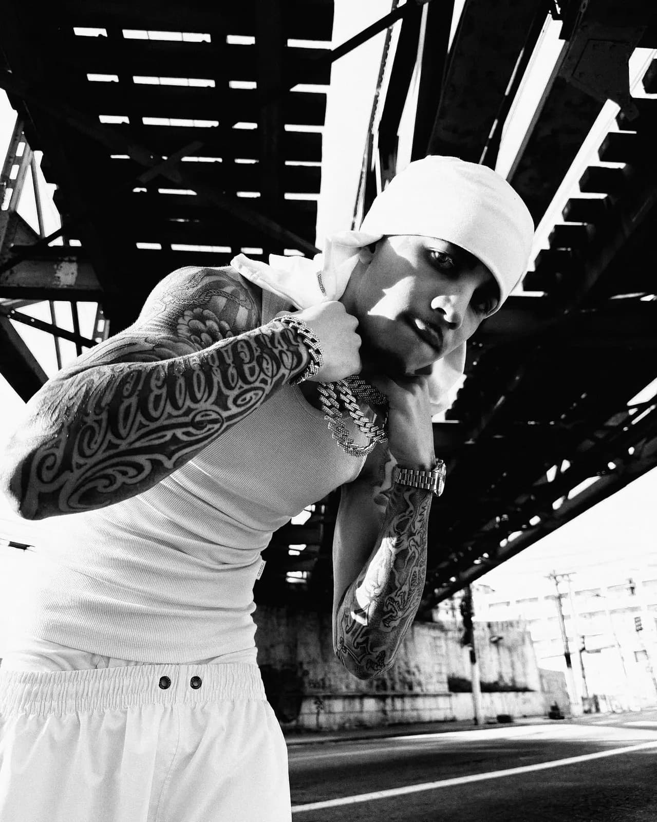 Bradockdan agachado debaixo do viaduto, com as tatuagens e as correntes à vista.